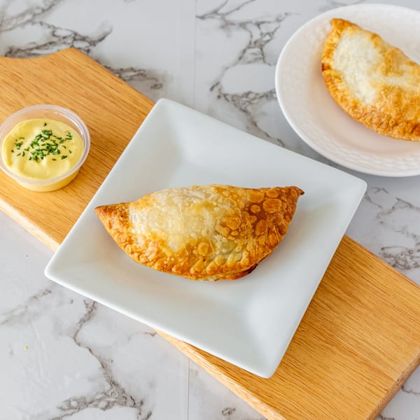 Two golden-brown Argentinian empanadas on white plates, with a side of dipping sauce.