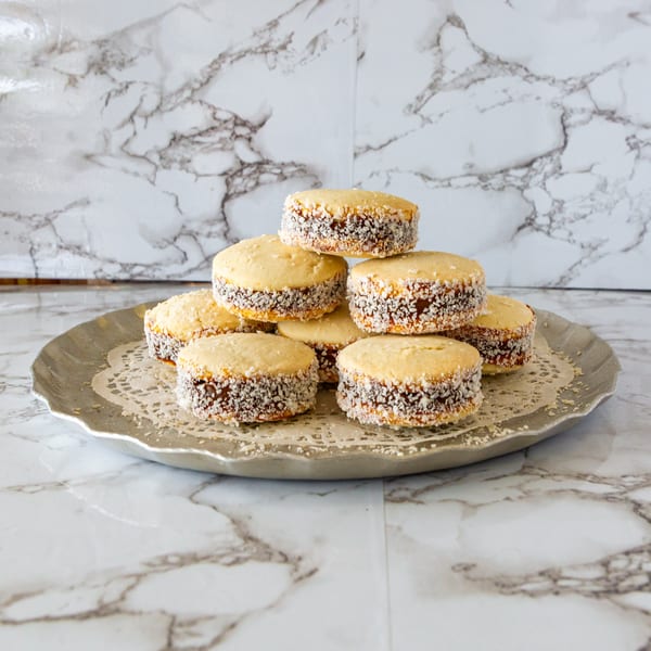 A pyramid of golden alfajores with dulce de leche and shredded coconut on a silver plate.