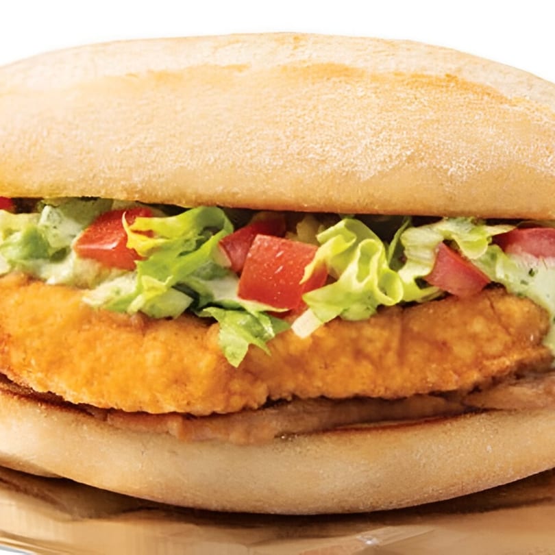 Close-up of a milanesa sandwich with crispy breaded steak, lettuce, diced tomatoes, and sauce.