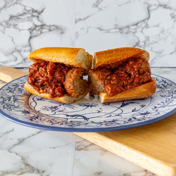 A meatball sub, cut in half, overflowing with rich red sauce on a decorative blue and white plate.