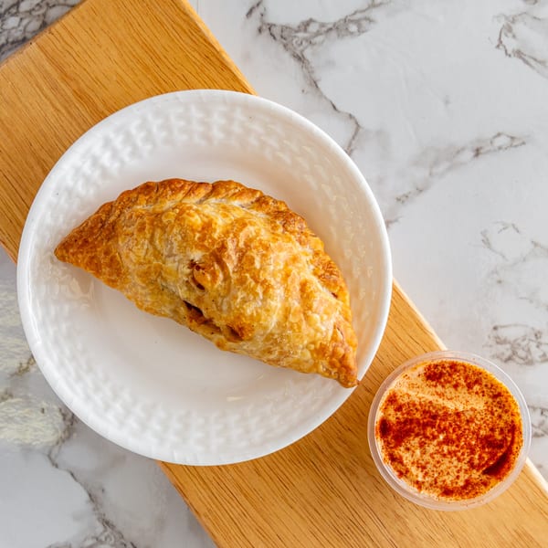 A golden-brown Argentinian empanada on a white plate, with a side of dipping sauce.