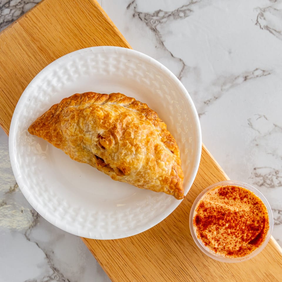 A golden-brown Argentinian empanada on a white plate, with a side of dipping sauce.