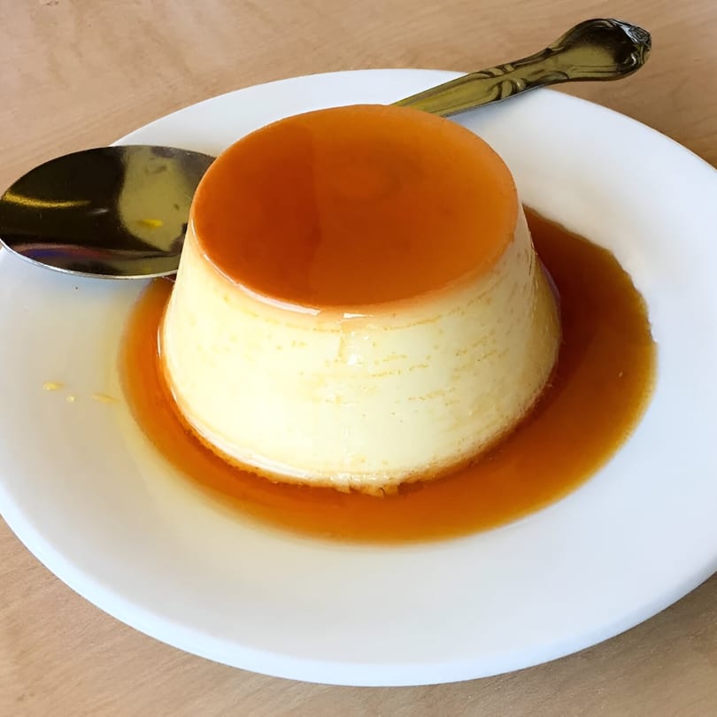 Flan dessert with rich caramel sauce on a white plate with a spoon, from Macanudo Mate.